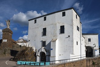 White painted historical building with a statue in the foreground under a blue sky, Santuario De