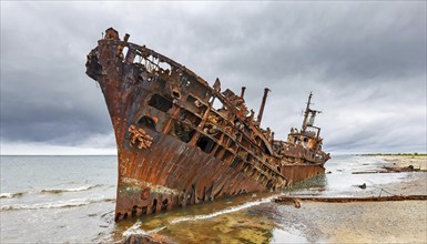 A rusty shipwreck lies on the beach under a cloudy sky in front of the sea, symbol photo, AI