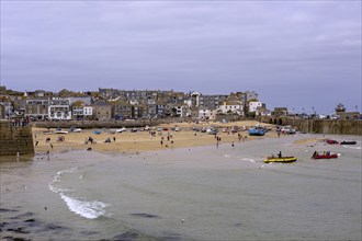 People enjoying the beach at low tide next to boats and buildings under a cloudy sky, town of St