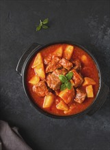 Stew with potatoes, in tomato sauce, with spices and herbs, close-up, no people, on a black