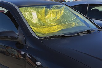 Car interior protected against heat buildup with foldable aluminum windshield sunshade and opened