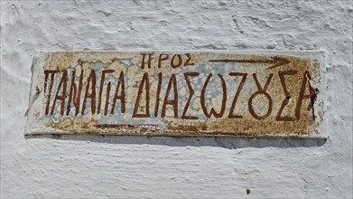 Sign Panagia Diasososuan, Weathered sign with Greek writing and an arrow on a white wall, Chora,