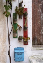 Flower pots with green plants hanging on wooden boards in the colours of Italy, blue post box,