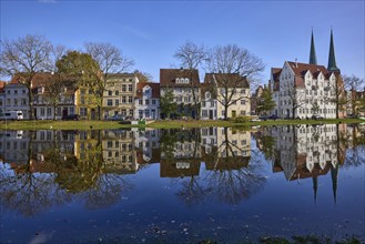 Riverbank of the Trave, historic houses, trees, church towers of Lübeck Cathedral, cloudless blue