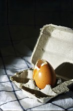 Cracked egg partially spilled on a checkered tablecloth, AI generated