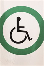 Close-up of posted white metal with black wheelchair in green circle Reserved Handicap Parking Spot