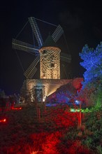 Old windmill at night, artistically illuminated in red and blue, surrounded by trees, world of