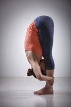 Beautiful sporty fit yogini woman practices yoga asana Uttanasana, standing forward bend pose