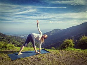 Woman doing Ashtanga Vinyasa yoga asana Parivrtta trikonasana, revolved triangle pose outdoors in