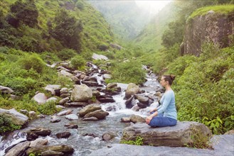 Woman in Hatha yoga asana Padmasana outdoors at tropical waterfall