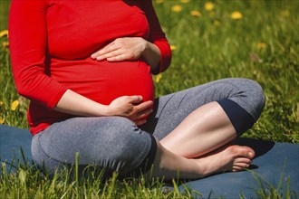 Pregnancy yoga exercise, pregnant woman doing asana Sukhasana easy yoga pose holding her abdomen