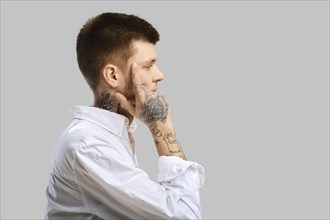 Young man touching his temple with a finger, standing in profile