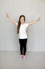 Cute young child with long hair in t-shirt and sweatpants standing with arms spread apart