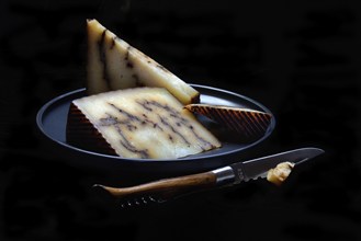 Sheep cheese with black garlic on plate with knife, Spain, Europe