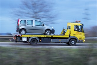 ADAC car transporter with loaded car driving on a country road, twilight, motion blur,