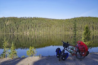 Bicycle standing by a crystal clear lake on an empty road, evening light, Stewart Cassiar Highway,