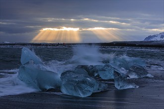 Waves breaking on icebergs on the black beach of Breidamerkursandur, sunset, near Jökullsarlon,