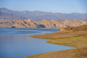 Blue Toktogul reservoir between dry mountain landscape, hilly mountains in the evening light,