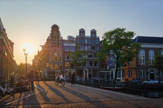 AMSTERDAM, NETHERLANDS, MAY 20, 2018: People on bicycles on Amsterdam bridge over canal with houses