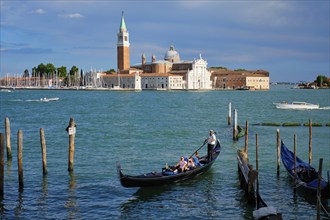 VENICE, ITALY, JUNE 27, 2018: Gondolier with tourists in gondola in lagoon of Venice by Saint Mark