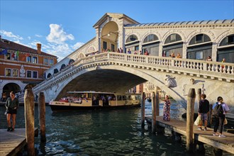 VENICE, ITALY, JUNE 27, 2018: Rialto bridge with vaporetto passing under on Grand Canal on sunset,