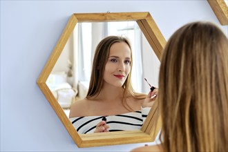 Pretty lady applying lipstick looking in the mirror