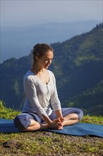 Sporty fit woman practices yoga asana Baddha Konasana, bound angle pose outdoors in HImalayas