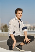 Young man in unfastened white shirt sits on squats on the street