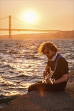 Hipster street musician in black playing electric guitar in street outdoors on sunset