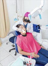 Dentist in his office examining female patient's mouth. Female dentist examining mouth to teen girl