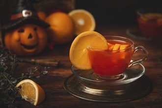 Tea with orange in cup, on wooden background, in front of Halloween decoration