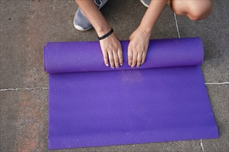 Woman hands rolling up the mat outside. Athlete woman hands rolling up the mat after exercising.