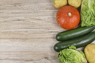 Healthy raw Hokkaido squash, zucchini, lettuce and potatoes on side of wooden background with empty