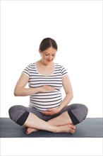 Pregnancy yoga exercise, pregnant woman doing asana Sukhasana easy yoga pose embracing her belly