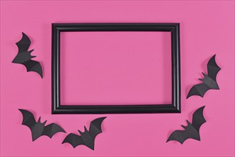 Halloween flat lay with black flying paper craft bats around empty picture frame on bright pink