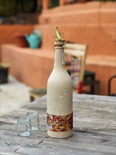 Bottle of mezcal with praying mantis (Mantis religiosa) and two glasses on a simple wooden table,