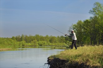 Man fish with spinning on river bank, casting lure. Outdoor weekend activity. Photo with shallow