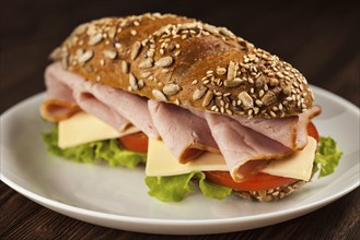 Ham sandwich with lettuce, cheese, tomato on plate on wooden table