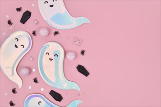 Cute pastel colored Halloween party flat lay with ghost shaped plates, coffins and confetti on pink