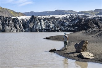 Tourist on the lakeshore of a glacier lagoon, glacier tongue and lake, Sólheimajökull, South