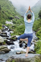 Woman in Hatha yoga balance yoga asana Vrikshasana tree pose at waterfall outdoors