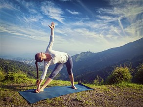 Woman doing Ashtanga Vinyasa yoga asana Utthita trikonasana, extended triangle pose outdoors in