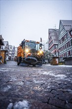 Clearing vehicle on a snow-covered road at a Christmas market at dusk, Black Forest, Calw, Germany,