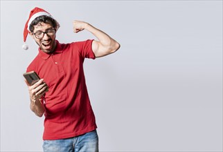 Smiling young man in christmas hat using cellphone celebrating. Happy guy in christmas hat looking