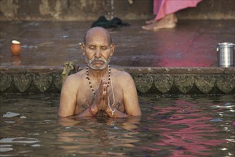 Indian man bathing and praying in the Ganges river at a ghat at Varanasi, Uttar Pradesh, India,