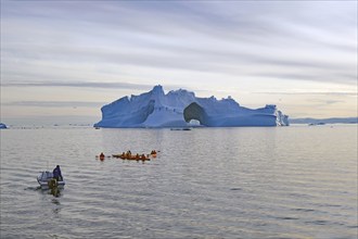 Small boat and kayaker in front of iceberg with large ice cave, Ilulissat, Disko Bay, Denmark,