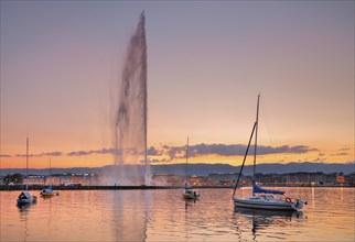 The Jet d'eau at dusk is the landmark in the Lake Geneva basin, with sailboats in the foreground