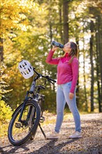 Woman on ebike drinking water bottle in autumn forest, Black Forest, Gechingen, Germany, Europe