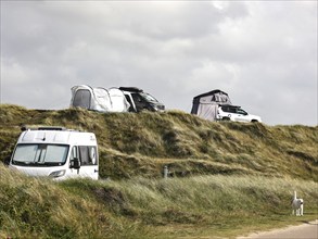 Motorhomes and an SUV with awning standing in the dunes of a campsite, Vejers, Denmark, 16.07.2023,