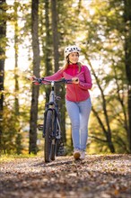 Woman pushing ebike through the autumn forest, Black Forest, Gechingen, Germany, Europe